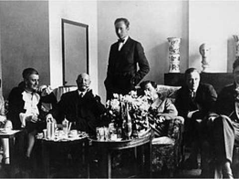 Wittgenstein sitting with his friends and family in Vienna. Marguerite Respinger sits at the end of the left and the sculpture he made of her sits behind him on the mantel-place