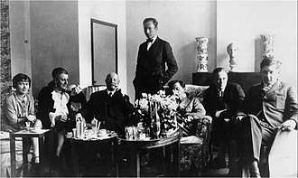 Wittgenstein sitting with his friends and family in Vienna. Marguerite Respinger sits at the end of the left and the sculpture he made of her sits behind him on the mantel-place