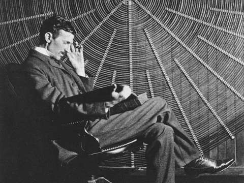 Tesla sitting in front of a spiral coil.