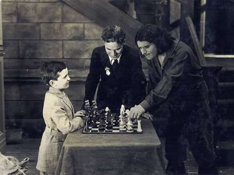Reshevsky playing chess with Douglas Fairbanks as Charlie Chaplin watches them during filming of the American silent film The Three Musketeers in 1921